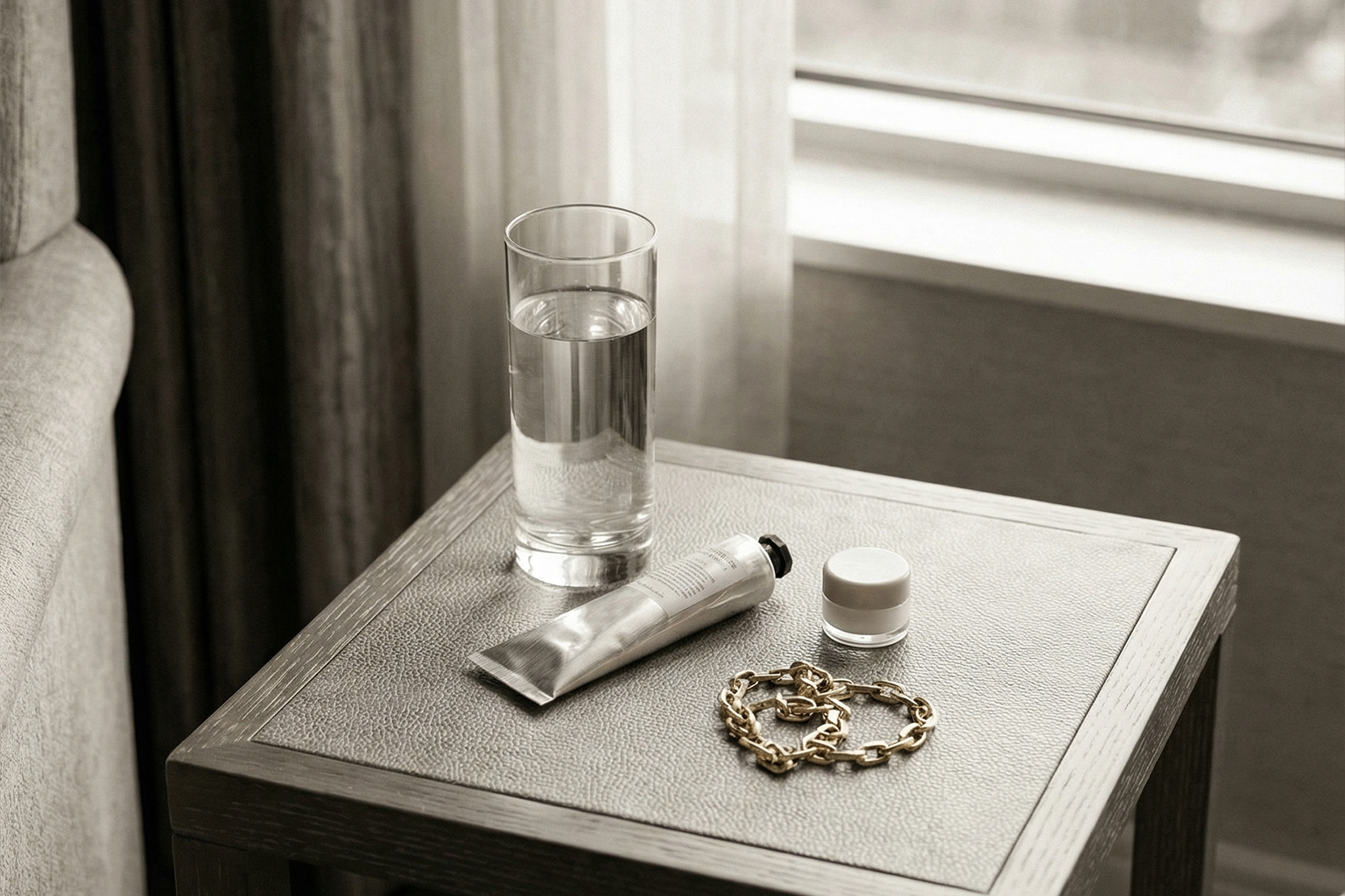 窓際のサイドテーブルに小型の加湿器と水、ハンドクリームが置かれた静かな室内。ニュートラルで上品。文字なし。