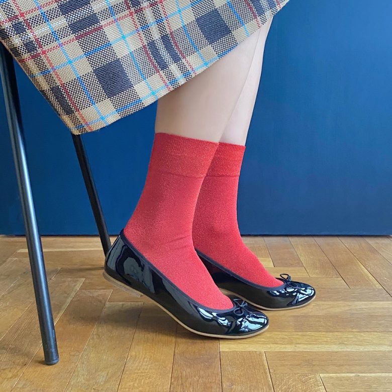 チェックスカートと赤ソックスに2021年12月10日発売の雑誌「CLUEL（クルーエル）」1月号で紹介されたラウンドトゥのフラットソールエナメルバレエシューズのブラックを合わせたトラッド風なコーデ